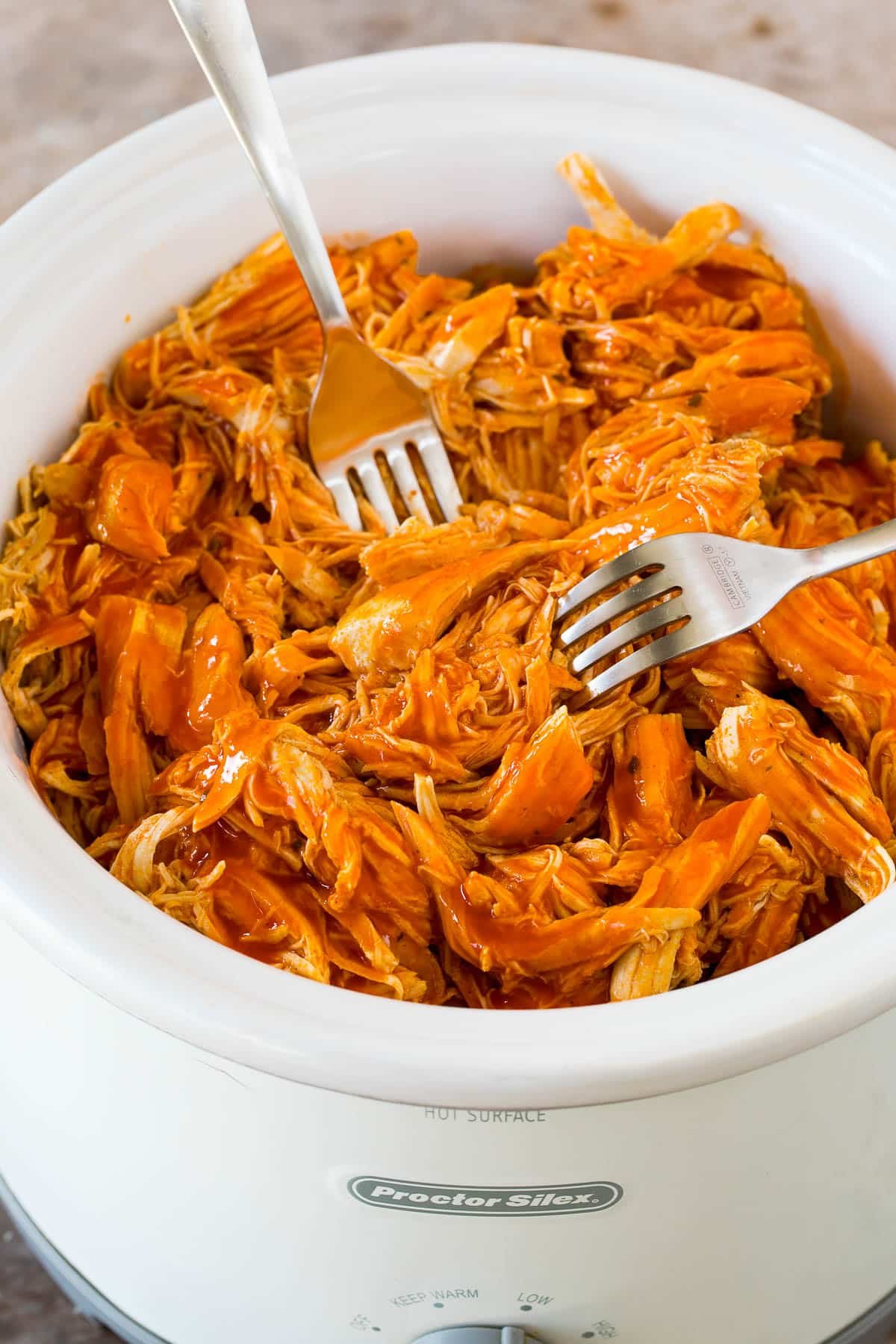 Two forks shredding chicken in a slow cooker.