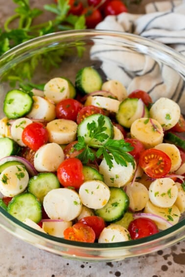 A serving bowl of hearts of palm salad garnished with a sprig of parsley.