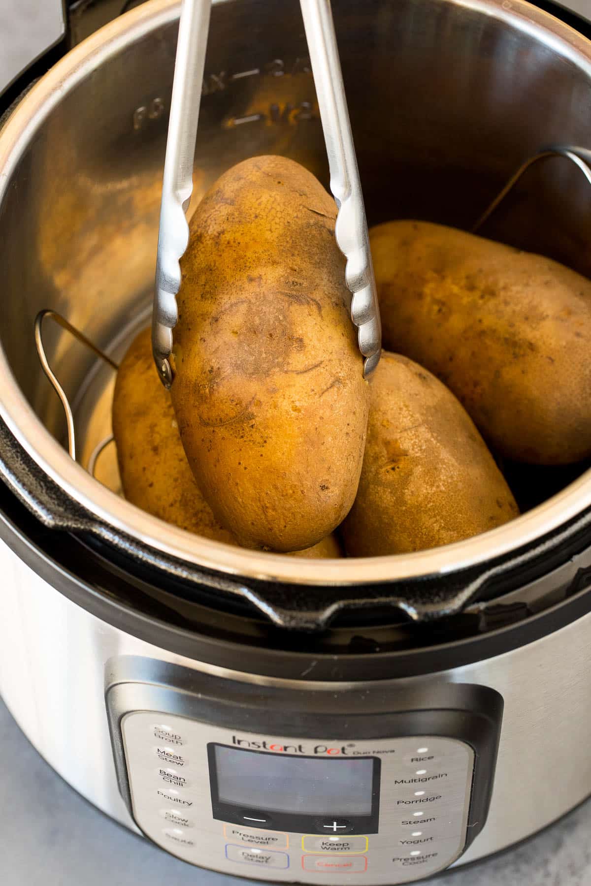Tongs removing a potato from an Instant Pot.