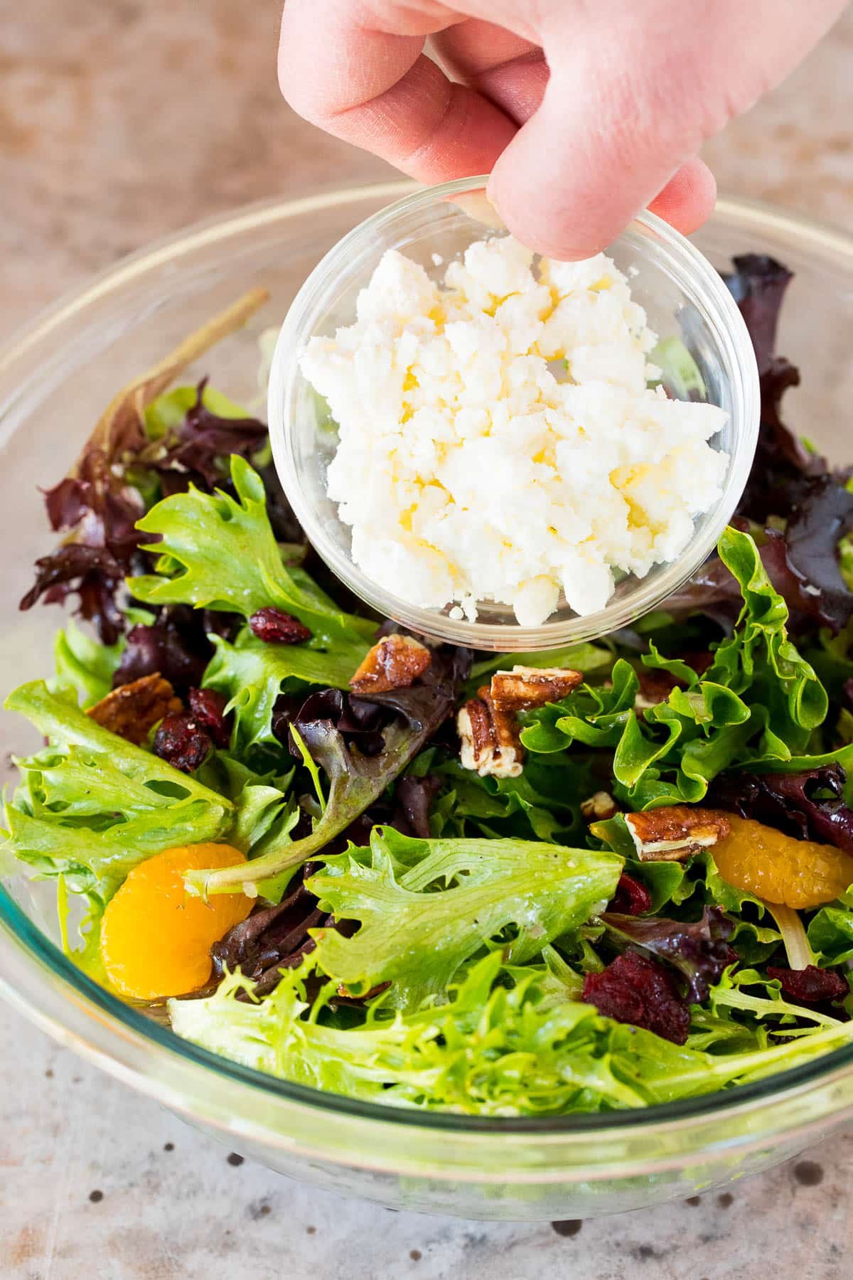 Feta cheese being poured over green salad.