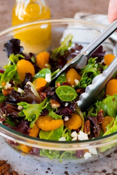 A bowl of mandarin orange salad with serving tongs in it.