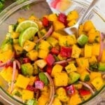 A bowl of mango salad with a serving spoon in it.