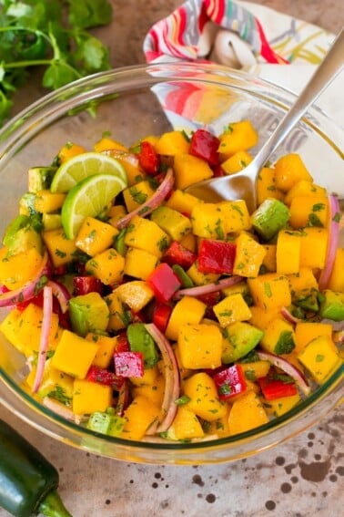 A bowl of mango salad with a serving spoon in it.