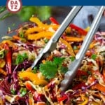 A bowl of Asian slaw which is a blend of cabbage, carrots, bell peppers, almonds and fresh herbs, all tossed in a homemade sesame ginger dressing.