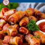 A plate of bacon wrapped smokies which are cocktail sausages wrapped in bacon, then coated in brown sugar and spices and baked to perfection.