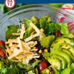 A bowl of Mexican salad which is mixed greens, black beans, tomatoes, corn, avocado, cotija cheese and tortilla strips all tossed in a tangy lime dressing.