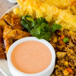 A bowl of yum yum sauce served with fried rice, chicken and tempura shrimp.