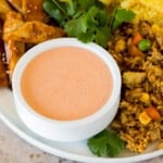 A bowl of yum yum sauce on a plate with fried rice and chicken.