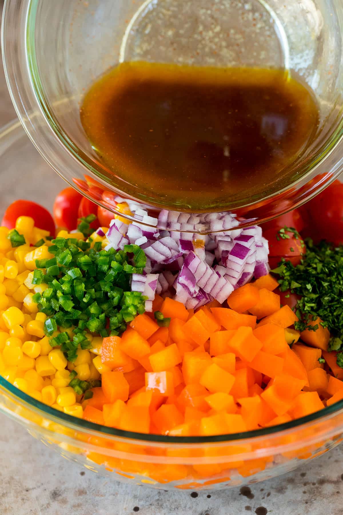 Dressing being poured over a bowl of vegetables.