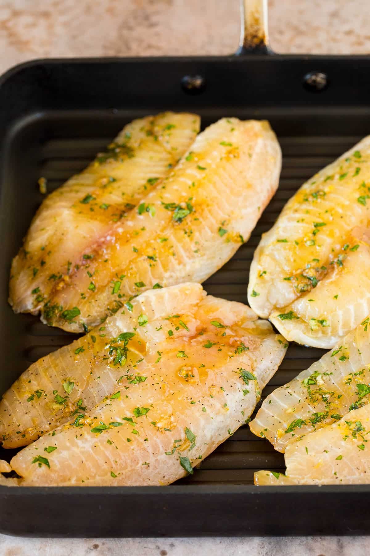 Marinated tilapia fillets on a grill pan.