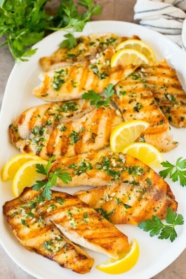 A platter of grilled tilapia fillets garnished with lemon and parsley.