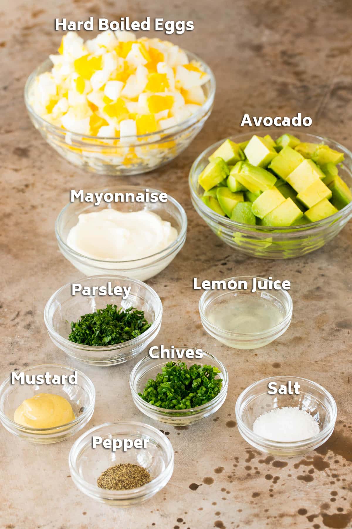 Bowls of ingredients including hard boiled eggs, avocado, seasonings and herbs.