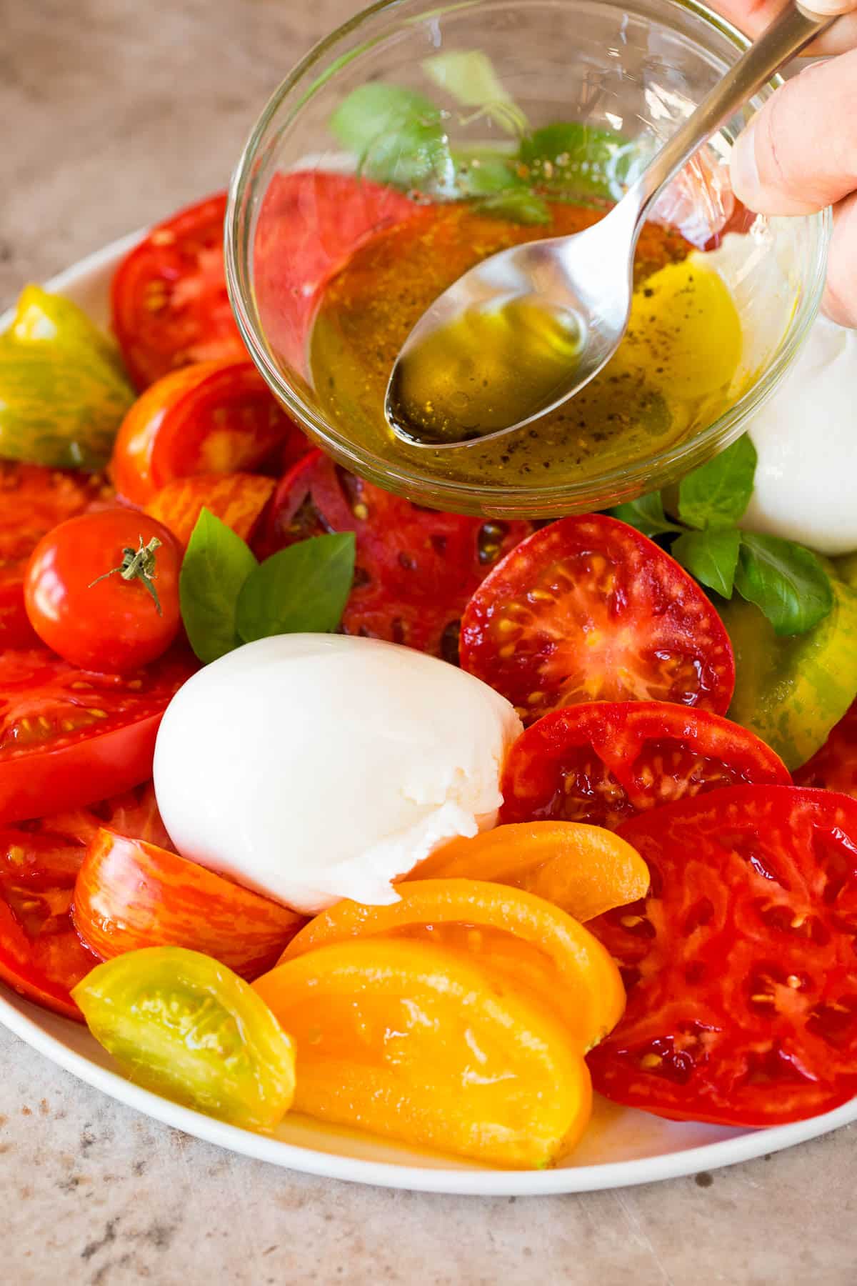 Dressing being poured over tomato and cheese salad.
