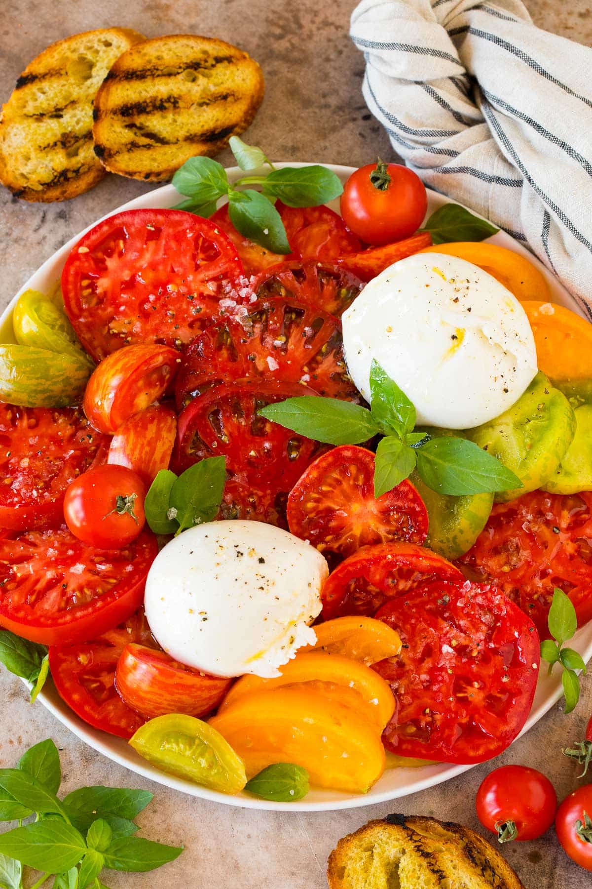 A platter of burrata salad with tomatoes, cheese, basil and dressing.