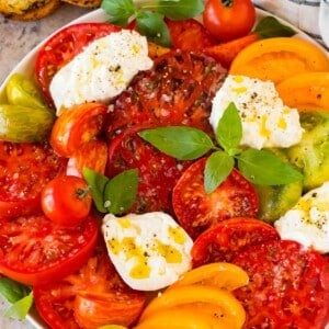 A serving plate of burrata salad with heirloom tomatoes, basil and lemon dressing.