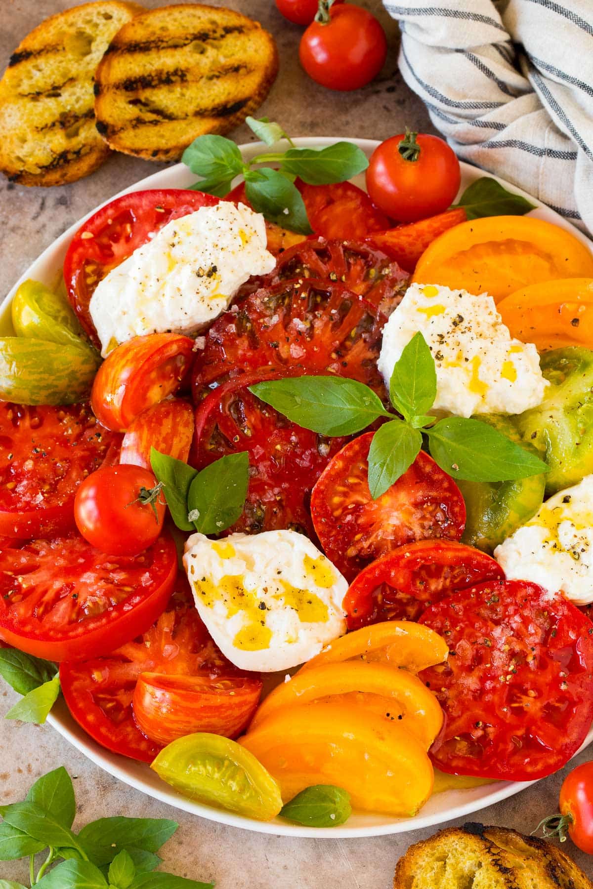 A serving plate of burrata salad with heirloom tomatoes, basil and lemon dressing.