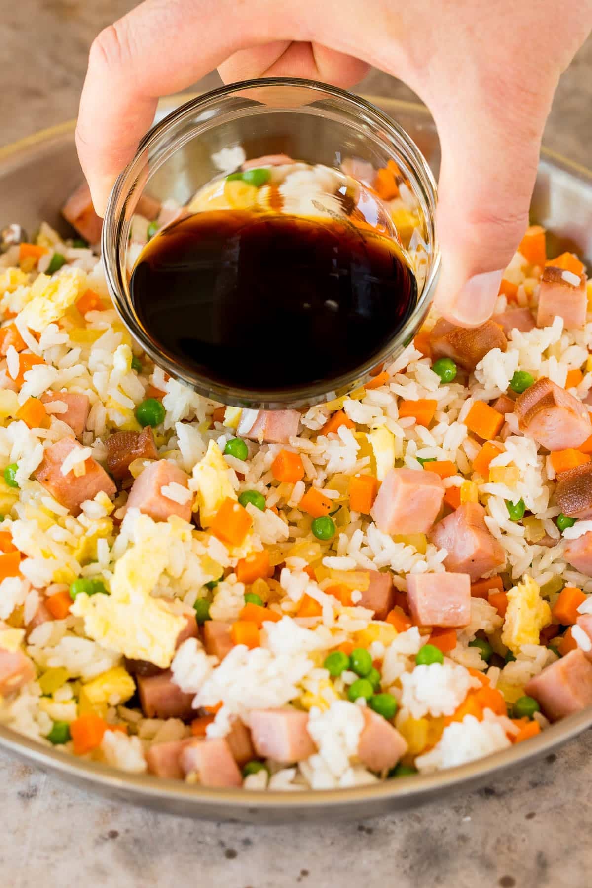 A bowl of sauce being poured over fried rice.