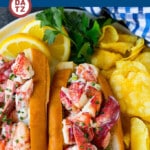 A plate with two lobster rolls and some potato chips.
