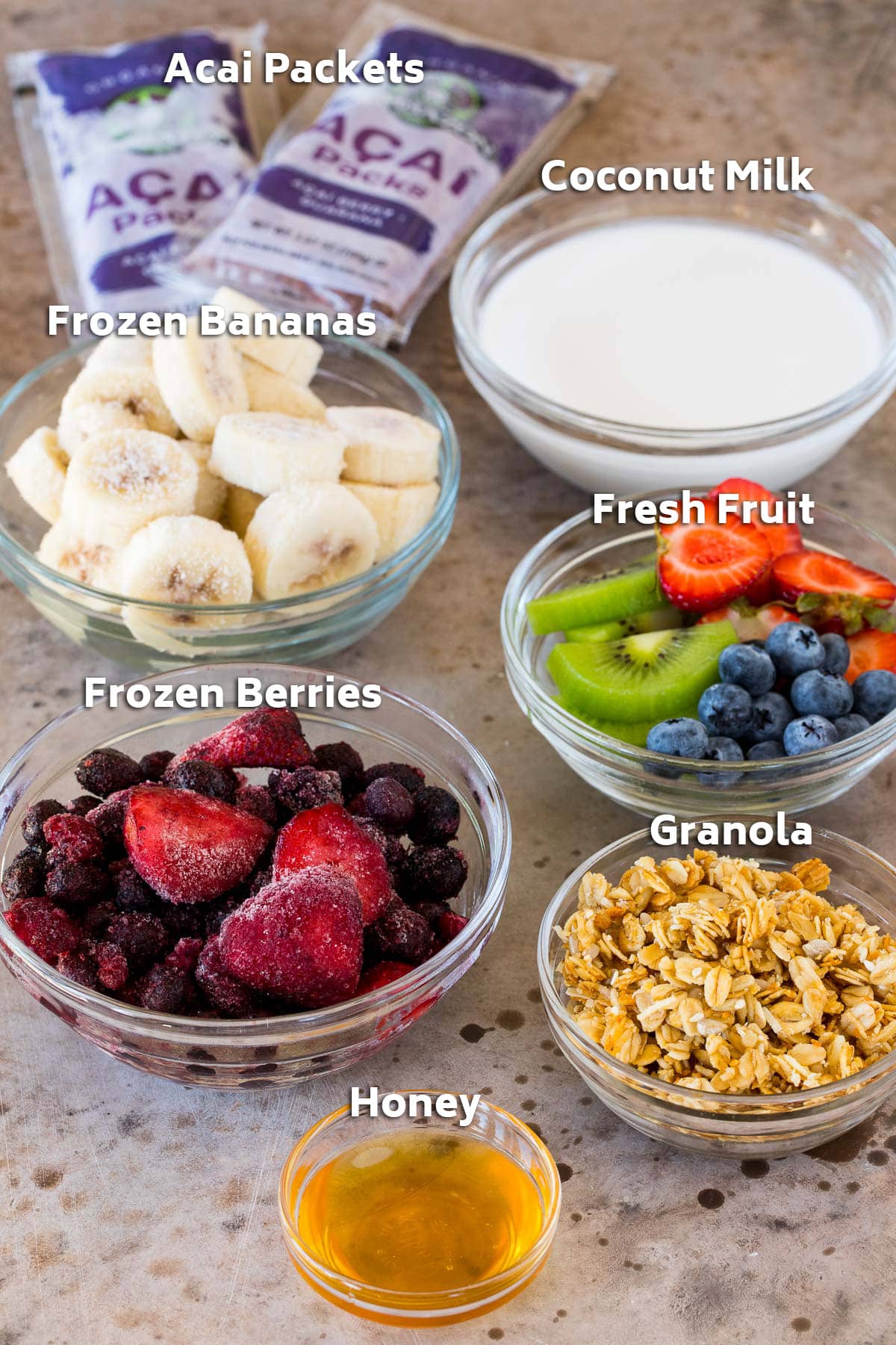 Bowls of ingredients including frozen fruit, coconut milk, honey and granola.