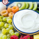 A bowl of cream cheese fruit dip on a plate surrounded by fruit.