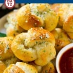 A plate of garlic knots next to a bowl of marinara sauce.