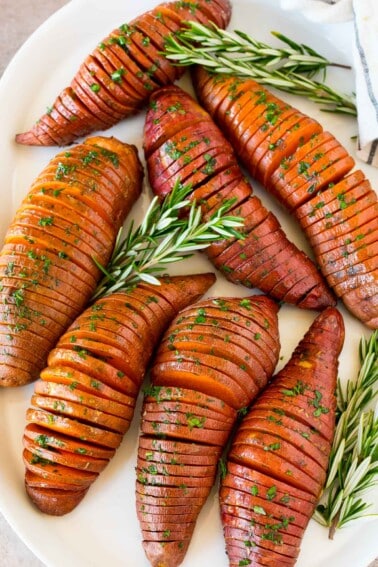 Hasselback sweet potatoes on a serving platter garnished with herbs.
