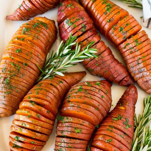 Hasselback sweet potatoes on a serving platter garnished with herbs.