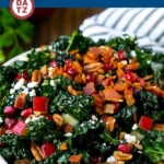 A bowl of kale salad with apples, pomegranate, bacon and feta cheese.