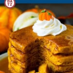 A plate of pumpkin pancakes with syrup and whipped cream.