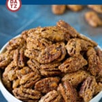A bowl of homemade candied pecans with a few pecans scattered around.
