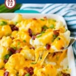 A baking dish with cauliflower casserole with melted cheese, bacon bits and green onions.