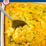 A baking dish full of corn pudding with a serving spoon taking a scoop.