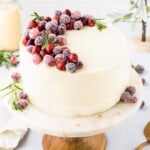 An eggnog cake on a cake stand garnished with fresh cranberries.