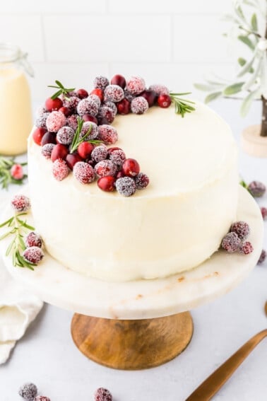 An eggnog cake on a cake stand garnished with fresh cranberries.