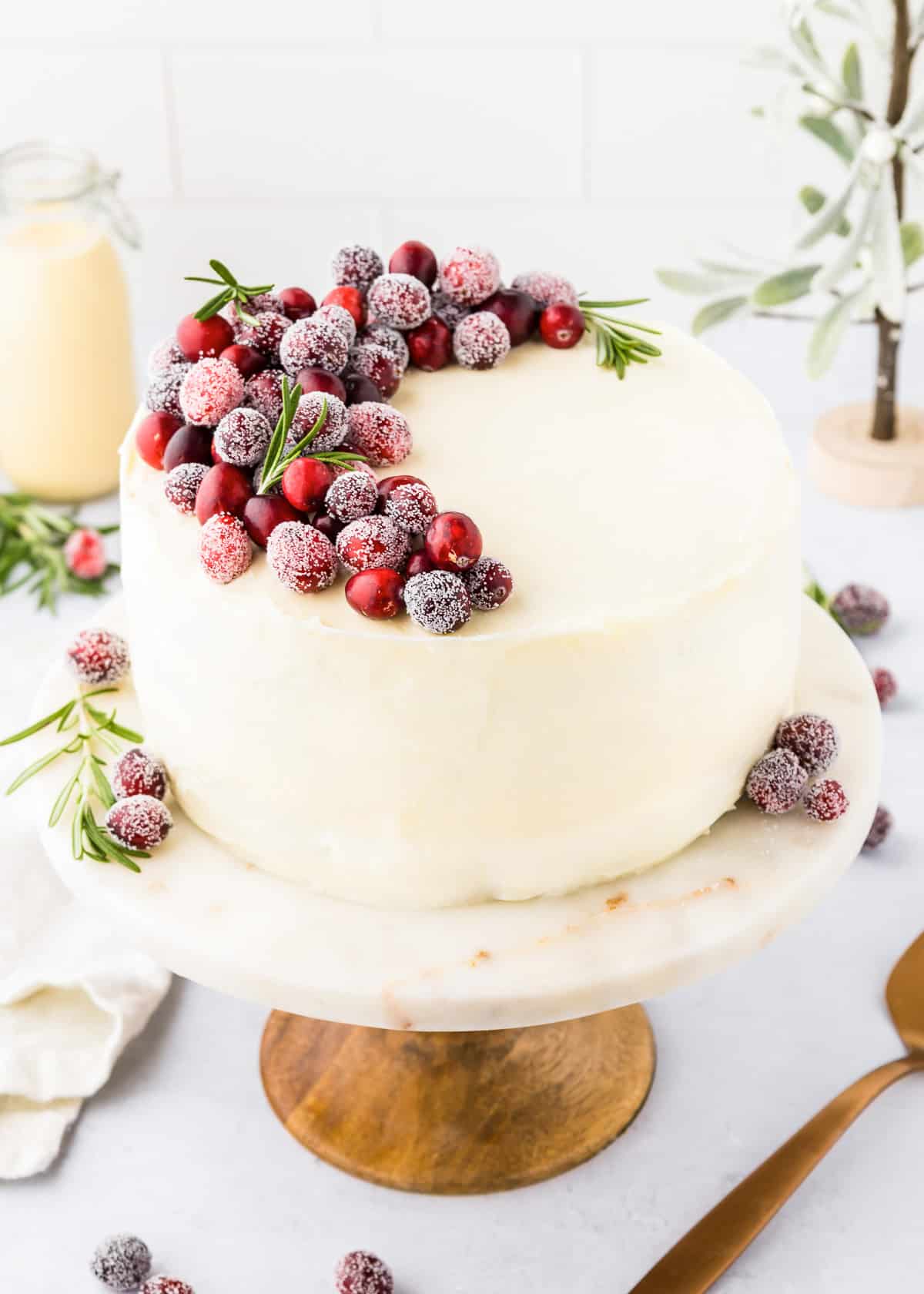 An eggnog cake on a cake stand garnished with fresh cranberries.