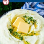 A bowl of garlic mashed potatoes with parsley and melted butter on top.