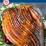 A glazed ham for the holidays on a serving platter garnished with cranberries and herbs.