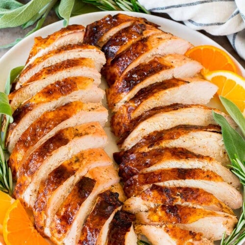 Sliced grilled turkey breast on a platter with herbs and citrus.