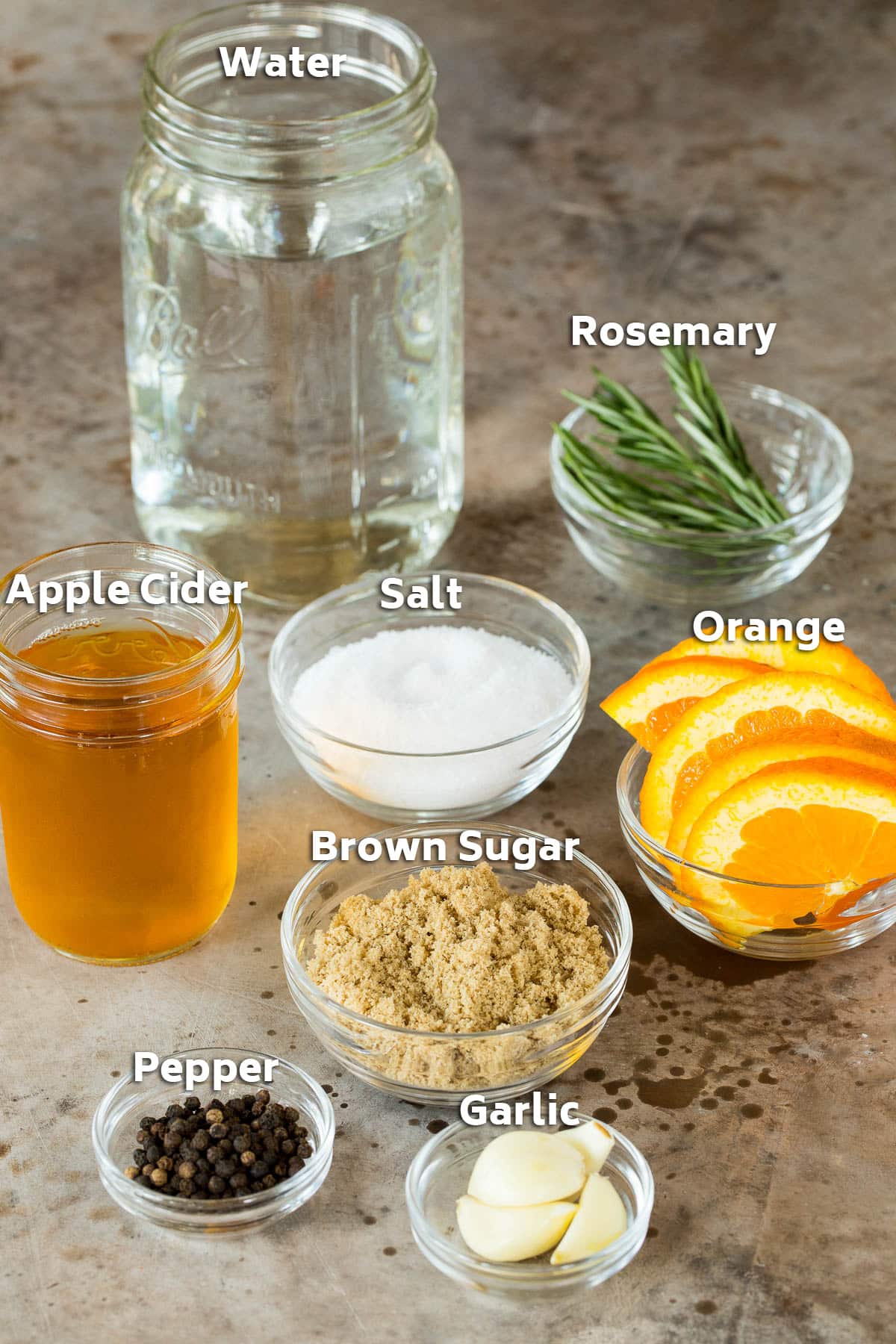 Bowls of ingredients for brine including salt, sugar, oranges and herbs.