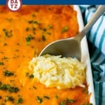 A baking dish with cheesy hashbrown casserole being scooped out with a serving spoon.