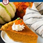 A slice of homemade pumpkin pie on a small plate with whipped cream and a pumpkin shaped candy on top.