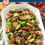 A serving dish of pomegranate brussels sprouts topped with pecans.