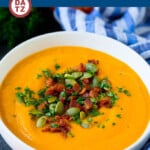 A bowl of pumpkin soup with bacon and pumpkin seeds on top.