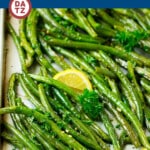 A sheet pan with roasted green beans garnished with parsley and lemon.