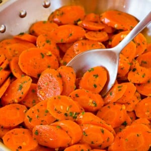 A pan of sauteed carrots with a serving spoon in it.