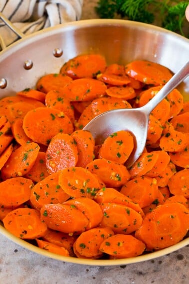 A pan of sauteed carrots with a serving spoon in it.