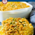 A plate of scalloped corn casserole on a small plate in front of a dish of casserole.