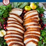 Sliced of roast turkey breast on a serving platter garnished with small apples and cranberries.