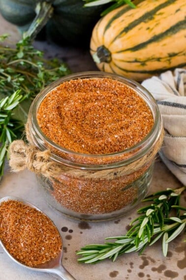 A jar of smoked turkey rub surrounded by herbs and winter squash.