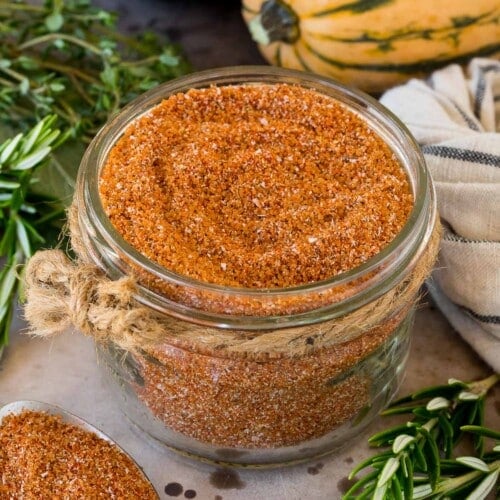 A jar of smoked turkey rub surrounded by herbs and winter squash.